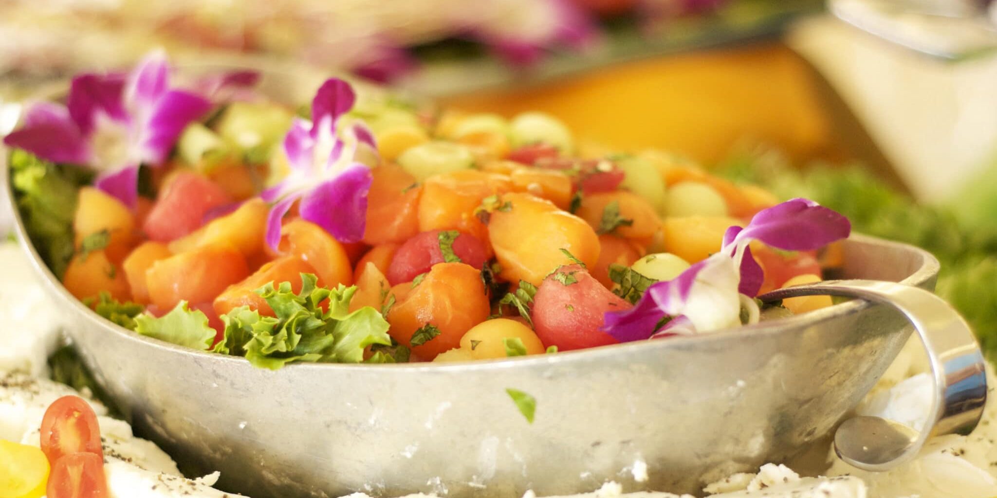 Catering A bowl of fruit with flowers in it.