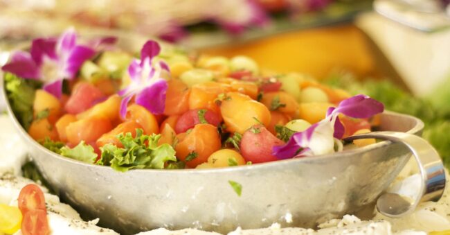 Catering A bowl of fruit with flowers in it.