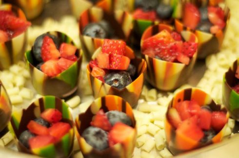 A close up of fruit in cups on top of white chocolate.